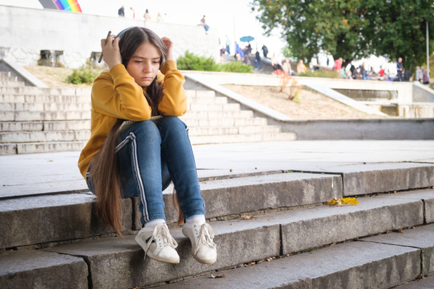 A sad teenage girl sits on the stairs and covers her head with her hands - Photo, Image