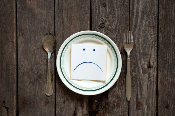 traurige Udibka auf einem Blatt Papier liegt auf einem leeren Teller auf dem Tisch, Traurigkeit, wenn es nichts zu essen gibt, Hunger und schlechte Laune - Foto, Bild