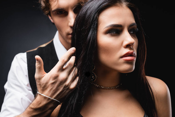 blurred man in vest and white shirt touching hair of brunette girlfriend on black - Fotografie, Obrázek