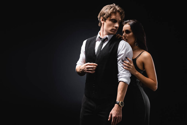 сексуальна жінка в ковзній сукні обіймає чоловіка в жилеті і сорочці на чорному
  - Фото, зображення
