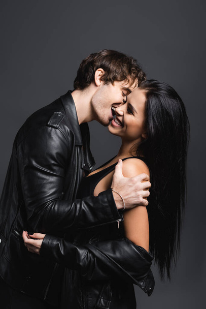 joyful and sexy couple in leather jackets laughing isolated on grey - 写真・画像