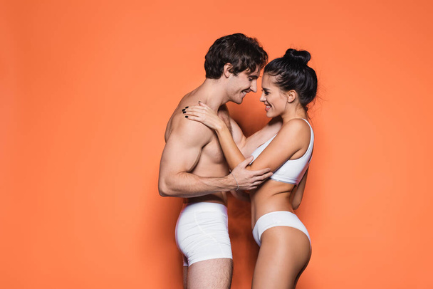 side view of happy and sexy couple in white underwear standing on orange - Fotografie, Obrázek