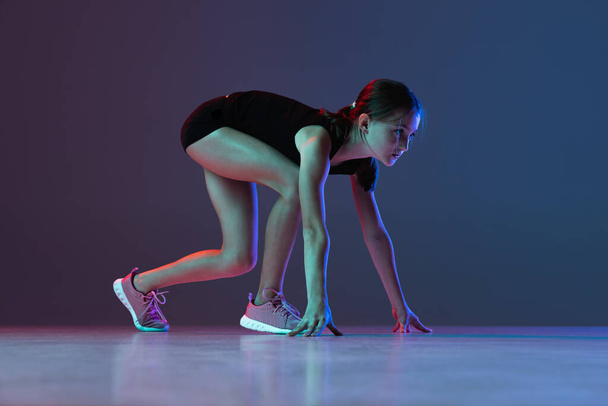 Retrato de cuerpo entero de adolescente, atleta en carrera preparándose para correr aislado sobre fondo azul púrpura degradado - Foto, imagen