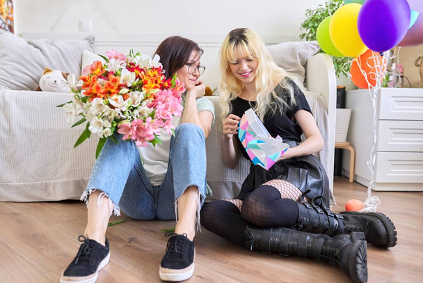 Mom and daughter happy teenage birthday girl with balloons flowers unpacking gift - Photo, Image
