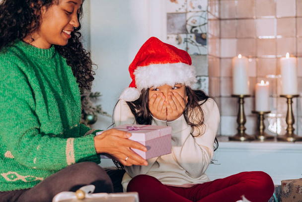 A lány és az anya karácsonyi kalapban ajándékokat bontanak ki. - Fotó, kép