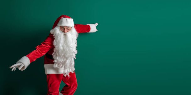 Emotional actor in costume of Santa Claus with long beard gestures and poses on green background - Foto, Imagen