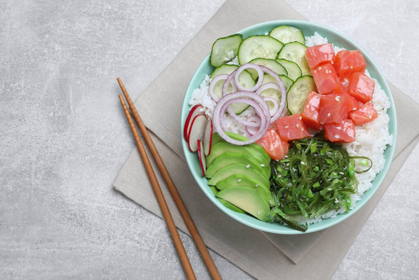 Delicious poke bowl with salmon, seaweed and vegetables served on light grey table, flat lay - Photo, image