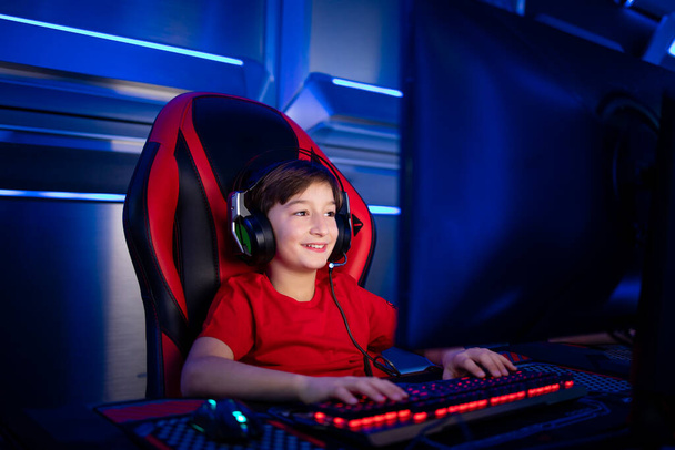 Мальчик с наушниками сидит в удобном кресле и играет в компьютерную видеоигру. - Фото, изображение