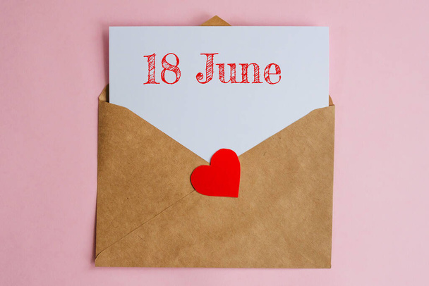 Kraft envelope with a white sheet of paper and a date 18 june, with red heart. Flat lay on pink background, romance and love concept - Foto, Imagem