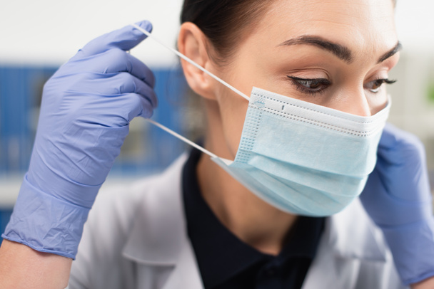 Brunette scientist in latex gloves wearing medical mask  - Foto, afbeelding