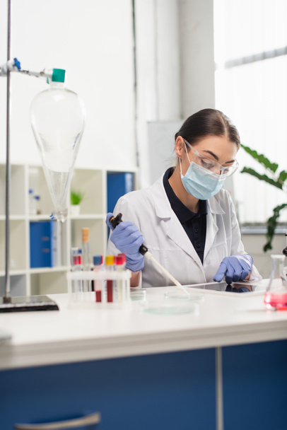 Scientist using digital tablet and holding electronic pipette near medical equipment in laboratory  - Photo, Image