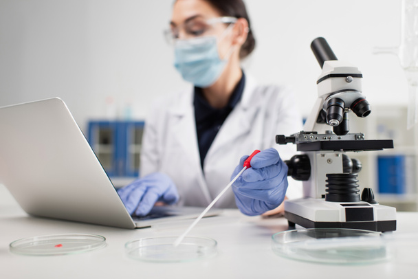 Vergrabener Wissenschaftler hält PCR-Test in der Nähe von Petrischalen und Laptop im Labor  - Foto, Bild