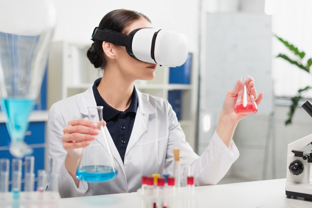 Scientifique en réalité virtuelle casque tenant des flacons près du microscope en laboratoire  - Photo, image