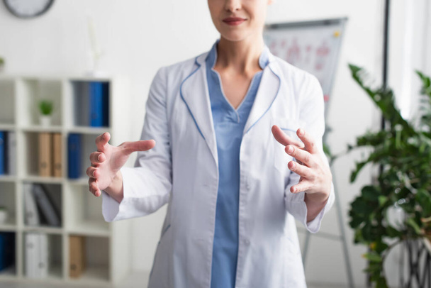 Oříznutý pohled na rozmazaného lékaře ukazujícího něco s rukama na klinice  - Fotografie, Obrázek