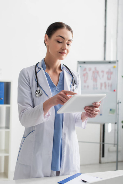 Brunette doctor with stethoscope using digital tablet in clinic  - Photo, Image