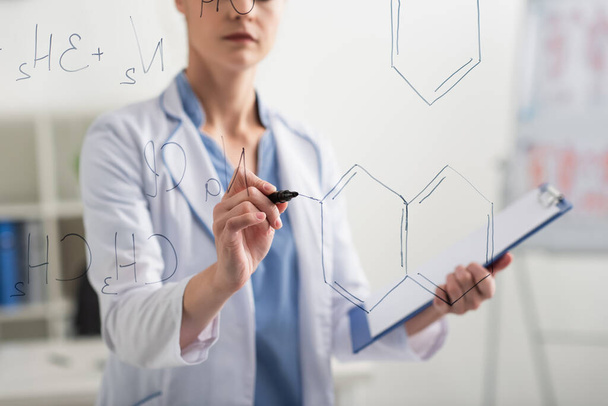 обрізаний вид розмитого лікаря з фетром для написання хімічних формул на скляній дошці
 - Фото, зображення