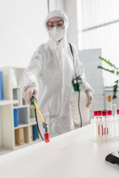 doctor borroso en traje protector haciendo desinfección de laboratorio con pulverizador - Foto, Imagen