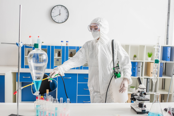 женщина в средств индивидуальной защиты делает дезинфекцию лаборатории с распылителем - Фото, изображение