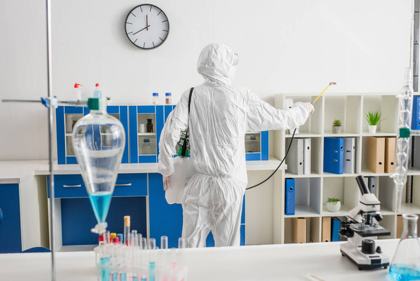 vista posterior del médico en traje de materiales peligrosos haciendo desinfección del laboratorio - Foto, Imagen
