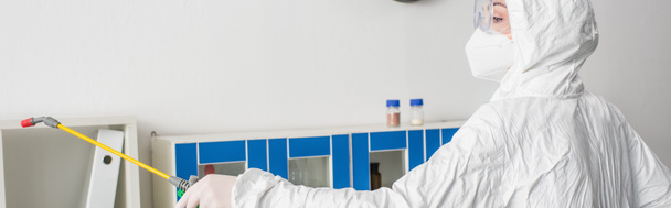 lekarz w okularach i kombinezonie ochronnym dezynfekujący laboratorium opryskiwaczem, bannerem - Zdjęcie, obraz
