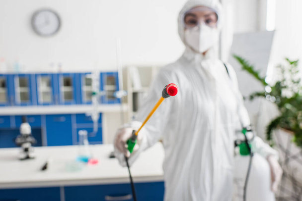 verschwommener Wissenschaftler im Schutzanzug hält Sprayer während Laborreinigung - Foto, Bild