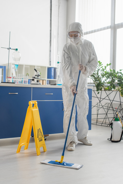 doctor en traje de materiales peligrosos limpieza piso con fregona en laboratorio médico - Foto, Imagen