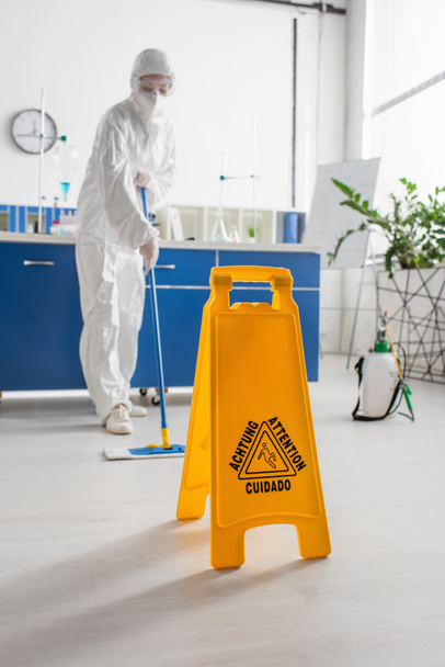 attention board near doctor in hazmat suit cleaning floor with mop - Foto, Bild