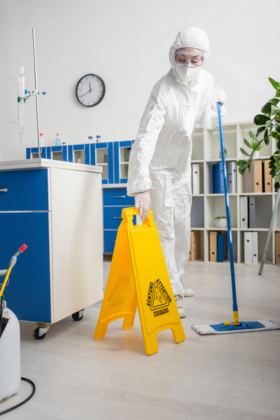 médico en traje de materiales peligrosos que sostiene la fregona y el tablero de atención mientras limpia el laboratorio - Foto, Imagen