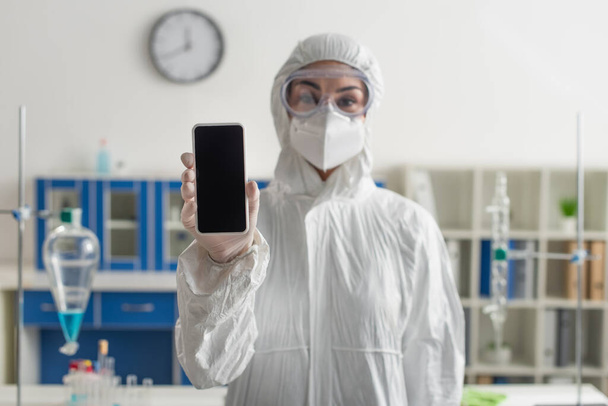blurred doctor in hazmat suit holding mobile phone with blank screen in lab - Фото, зображення
