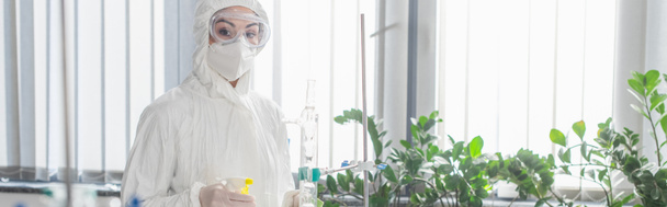 scientist in hazmat suit looking at camera while holding spray bottle, banner - Foto, immagini