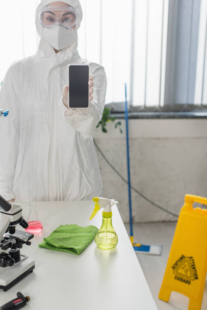 Wissenschaftler in Warnanzug und Schutzbrille zeigt Smartphone mit leerem Bildschirm im Labor - Foto, Bild