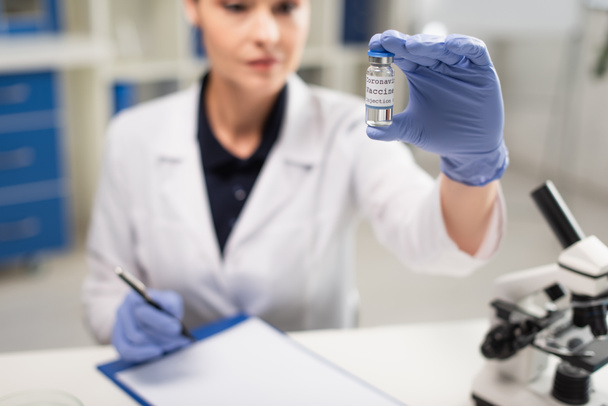 θαμπός γιατρός με γάντια λατέξ που κρατά το εμβόλιο του κορωναϊού στην κλινική - Φωτογραφία, εικόνα
