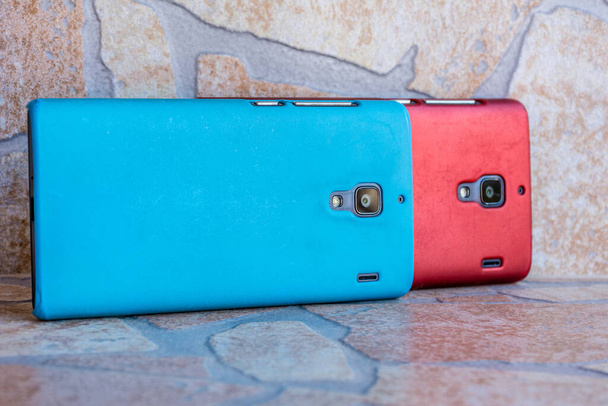 A closeup shot of two smartphones with red and blue cases on the stone surface - Foto, Bild
