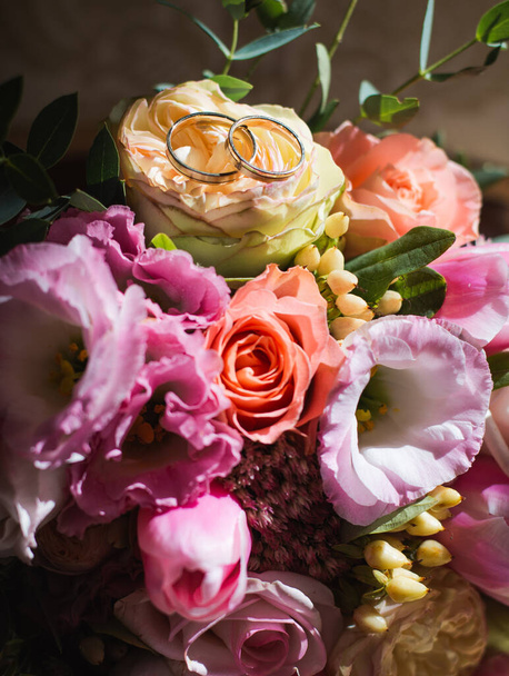 A vertical shot of a beautiful floral bridal bouquet with wedding rings on it - 写真・画像
