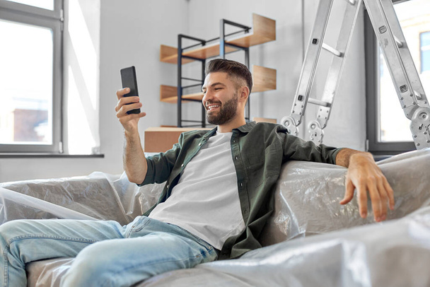 smiling man with smartphone moving into new home - 写真・画像