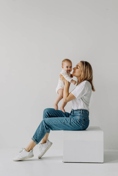 Mother holding baby in arms, smiling and playing, on white wall background. - Foto, Bild
