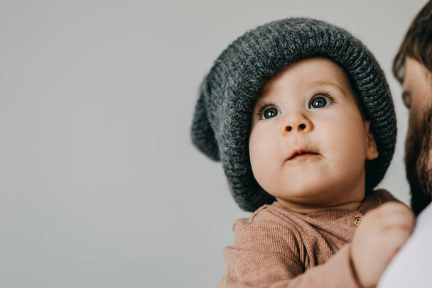 Baby wearing a gray oversized knitted beanie, on white wall background. - Fotografie, Obrázek