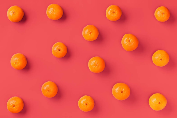 Fruit pattern of fresh orange tangerine or mandarin over living coral background. Flat lay, top view. Pop art design, creative summer concept. Citrus in minimal style. - 写真・画像
