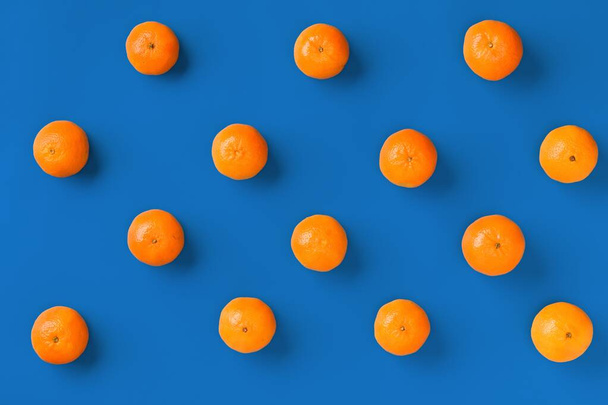 Fruit pattern of fresh orange tangerine or mandarin on blue background. Flat lay, top view. Pop art design, creative summer concept. Citrus in minimal style. - 写真・画像