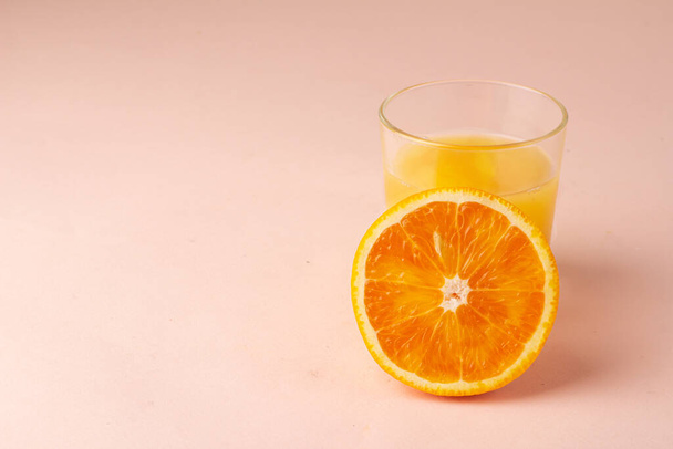 ピンクの背景にオレンジジュースとオレンジのスライス - 写真・画像