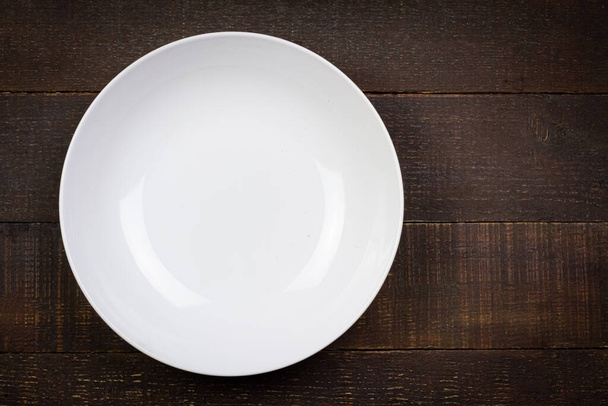 Λευκό άδειο πιάτο ξύλινο φόντο, Κάτοψη. Πιάτο από κεραμικό. Εξαίσια επιτραπέζια σκεύη. - Φωτογραφία, εικόνα
