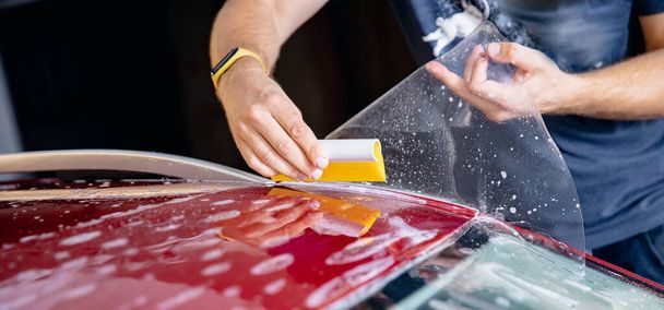 Master man instala tira de película de vinilo en zona de riesgo de parabrisas para proteger la pintura de la carrocería del coche de arañazos y virutas - Foto, imagen