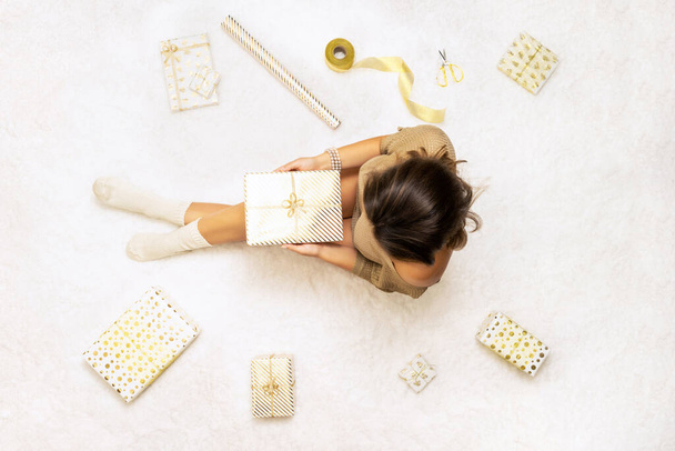 Female wrapping christmas gifts boxes for family sitting on fluffy snow-white carpet. Top view. - 写真・画像