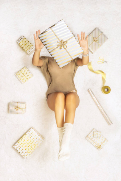 Mujer feliz vomitando una caja de regalo que se encuentra entre los regalos de Navidad de envoltura para la familia en la alfombra esponjosa blanca como la nieve. Vista superior. - Foto, imagen