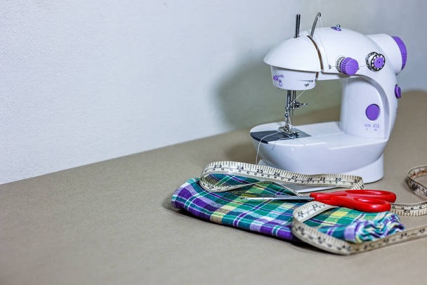 Máquina de costura, tecido, tesoura e guia de medição na mesa. Conceito de alfaiataria ou vestuário artesanal. - Foto, Imagem