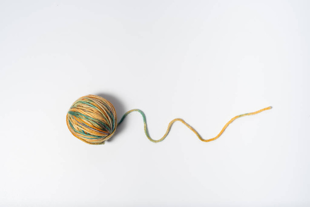 Piccola palla di filato multicolore chiaro con una stringa allentata su sfondo bianco - Foto, immagini