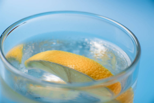 Lemon slice in a glass of fresh water on a blue background close-up close-up. - Фото, изображение