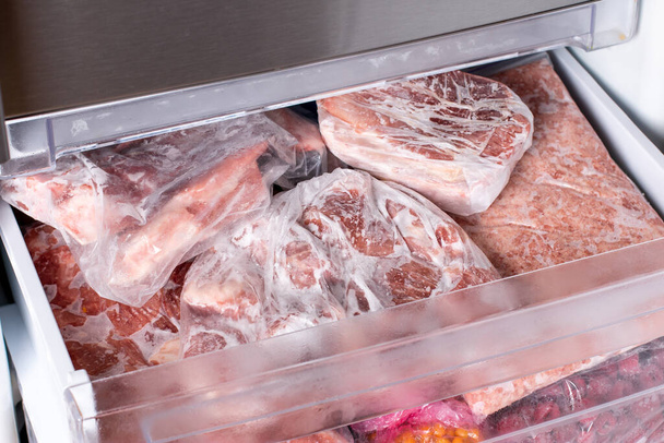 Meat in refrigerator freezer background. Closeup pork, meat and chicken leg in freezing compartment. Frozen food - Photo, Image