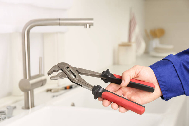 Plumber with spanner near sink in kitchen, closeup. Water tap installation - Photo, image