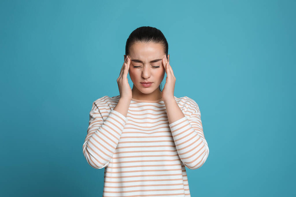 Молодая женщина страдает от головной боли на светло-голубом фоне - Фото, изображение